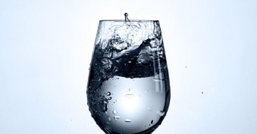 Bubbles of drinking water falling in the wineglass standing on the glass with droplets against light background. Pure and clear water. Environmentally friendly product. Care for the environment and health. Healthy lifestyle.